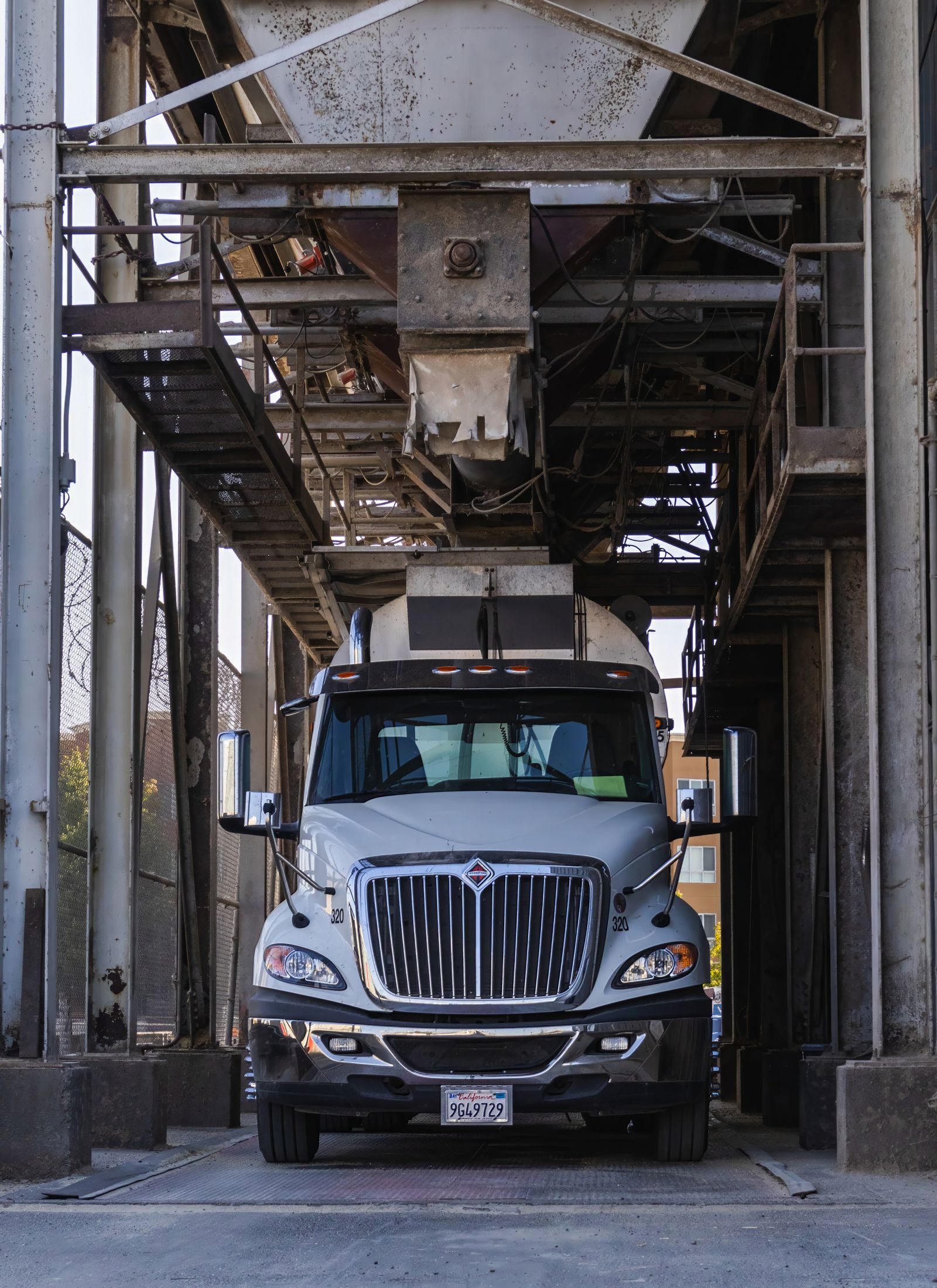 A white day-cab truck positioned under an industrial loading chute